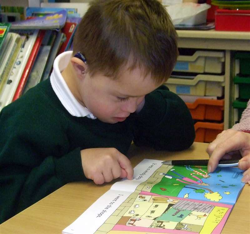 A photograph of a boy with Down syndrome learning to read a book