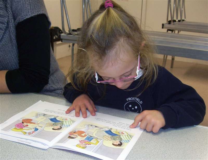 A photograph of a girl with Down syndrome learning to read a book.